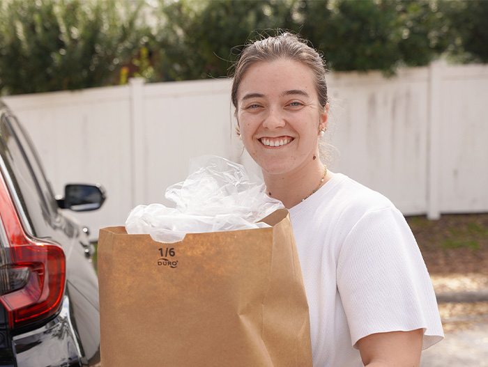 Smiling woman loading bag of food into car trunk