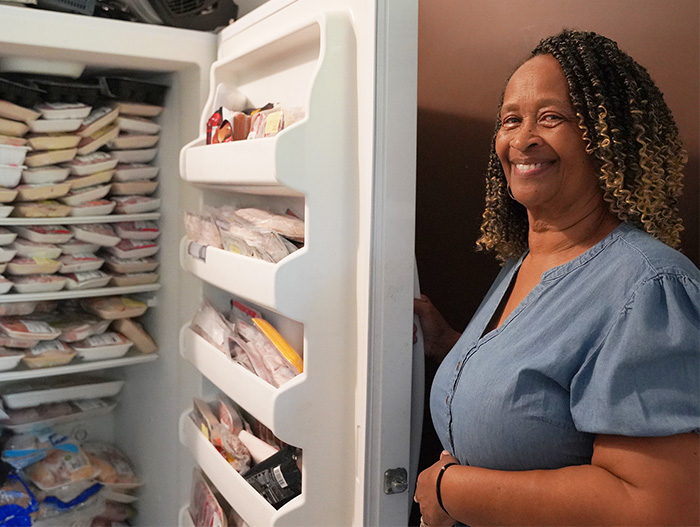 Woman standing next to open fridge filled with food
